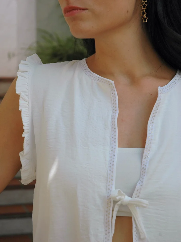 Chaleco blanco sin mangas Wheel con volantes en hombros y lazo frontal. Diseño ligero y femenino, ideal para looks de verano con estilo relajado.
