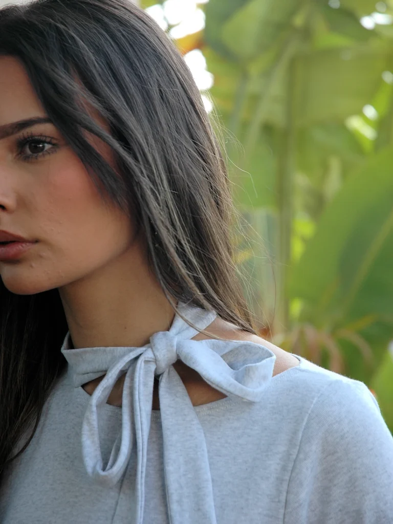Camiseta gris claro cropped con cuello alto y tira anudada. Diseño minimalista y elástico, ideal para looks urbanos, oficina o conjuntos actuales.