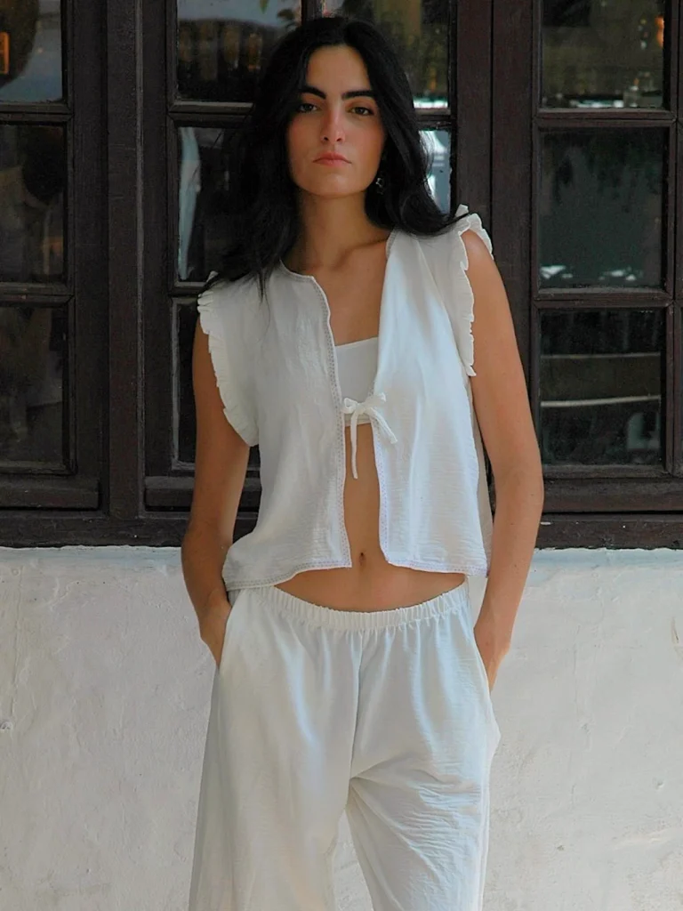 Chaleco blanco sin mangas Wheel con volantes en hombros y lazo frontal. Diseño ligero y femenino, ideal para looks de verano con estilo relajado.