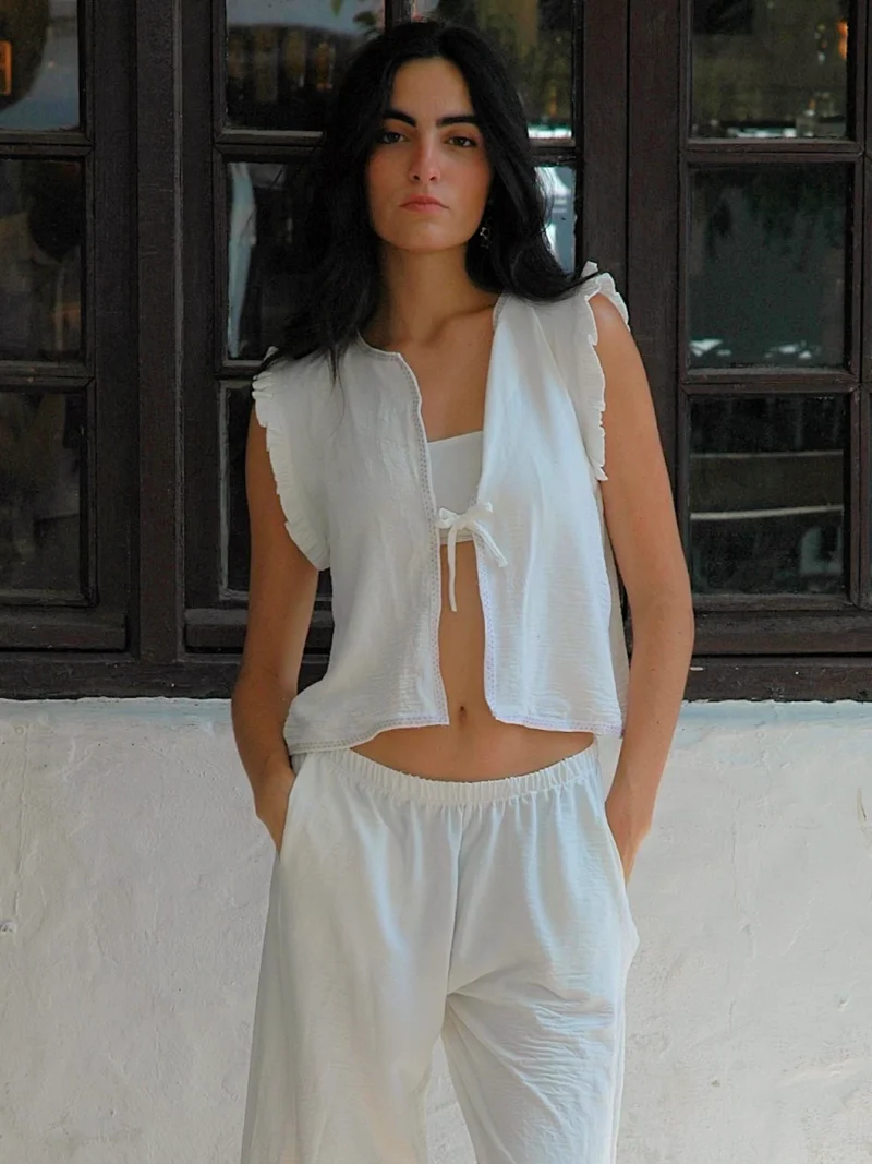 Chaleco blanco sin mangas Wheel con volantes en hombros y lazo frontal. Diseño ligero y femenino, ideal para looks de verano con estilo relajado.