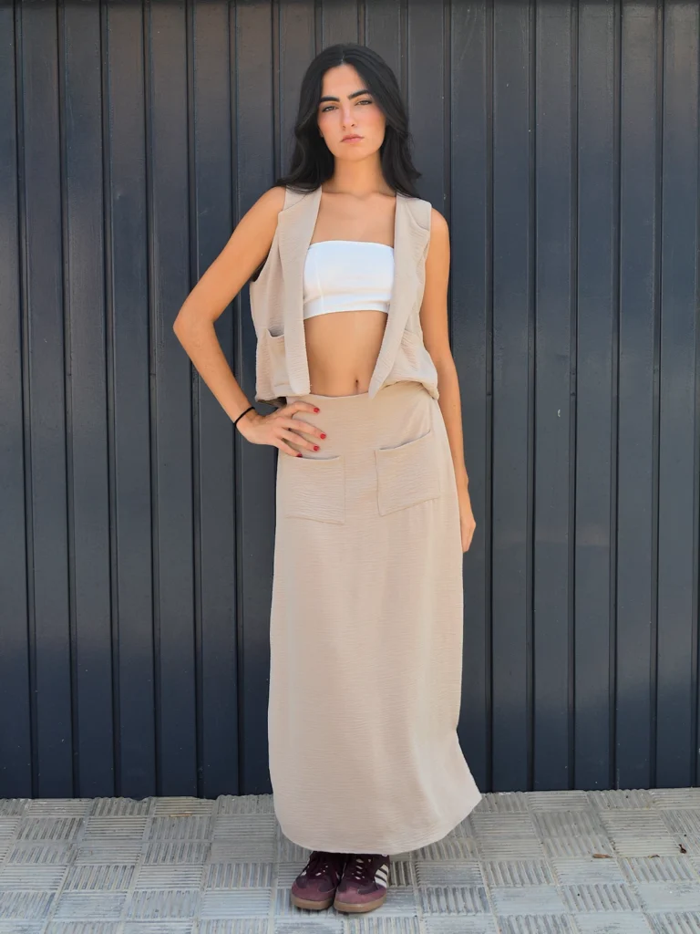 Chaleco beige arena sin mangas con solapas clásicas y bolsillos delanteros. Diseño elegante y versátil ideal para looks de oficina y estilismos casual chic.