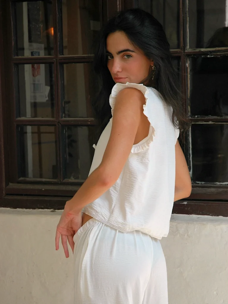 Chaleco blanco sin mangas Wheel con volantes en hombros y lazo frontal. Diseño ligero y femenino, ideal para looks de verano con estilo relajado.