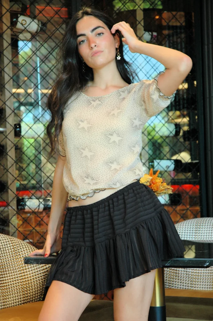 Falda corta negra Hadita con gasa semitransparente y volante. Diseño con volumen y cinturilla elástica, ideal para looks elegantes o casuales.