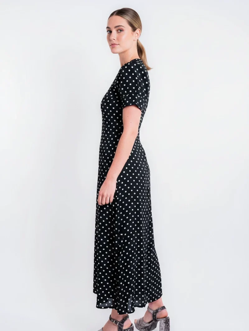 Vestido midi negro de lunares con manga corta y tejido fluido. Diseño atemporal ideal para oficina, eventos y looks diarios elegantes.