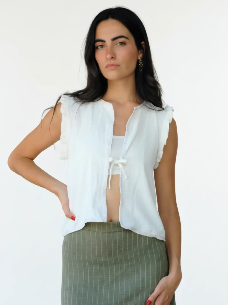Chaleco blanco sin mangas Wheel con volantes en hombros y lazo frontal. Diseño ligero y femenino, ideal para looks de verano con estilo relajado.