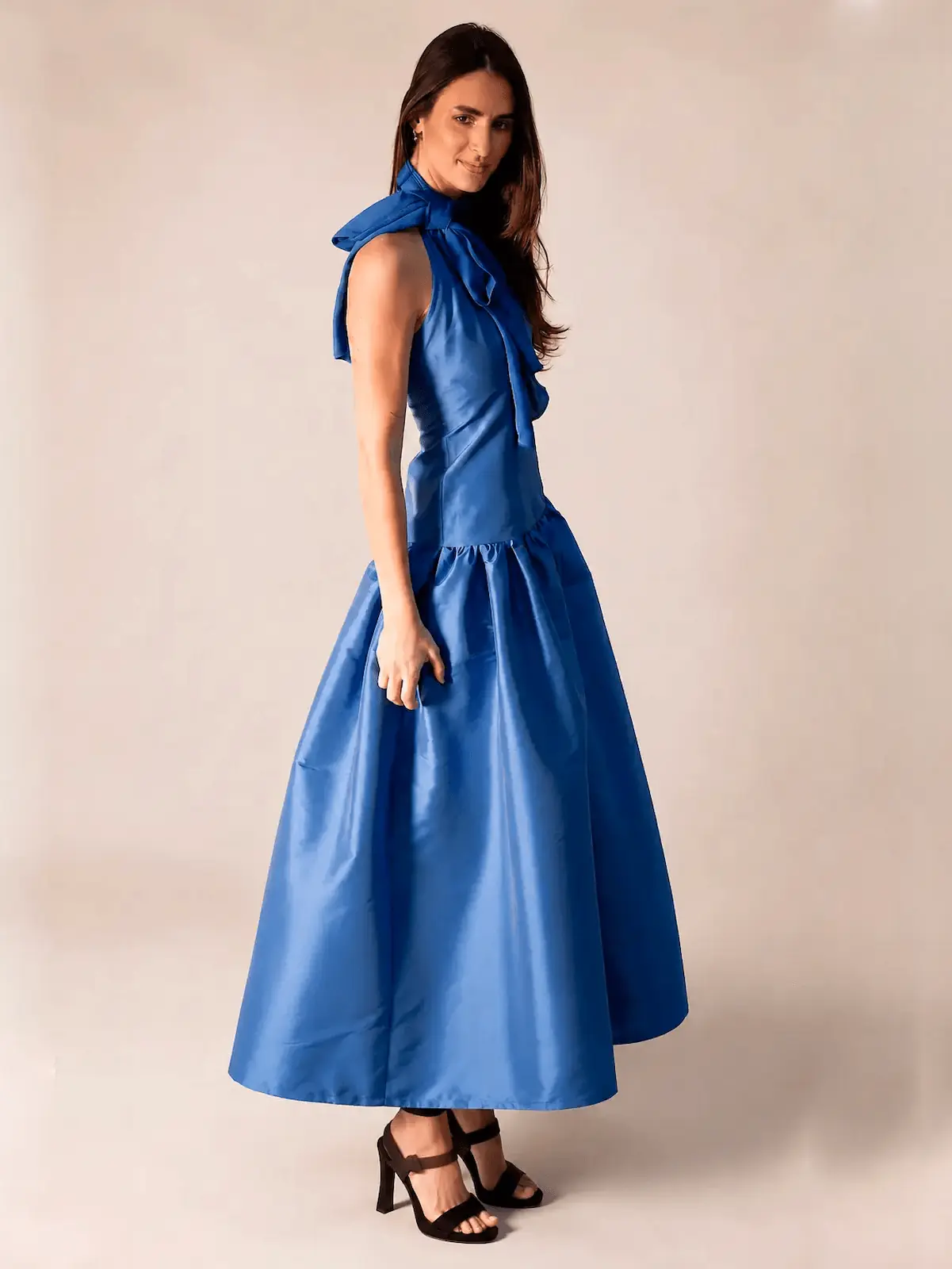 Vestido largo azul marino en tafetán con cuello halter y lazada. Su cuerpo estilizado y su amplia falda con volumen crean una silueta elegante y sofisticada, perfecta para bodas, graduaciones y eventos especiales.