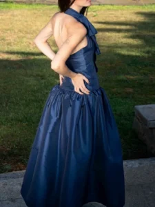Vestido largo azul marino en tafetán con cuello halter y lazada. Su cuerpo estilizado y su amplia falda con volumen crean una silueta elegante y sofisticada, perfecta para bodas, graduaciones y eventos especiales.