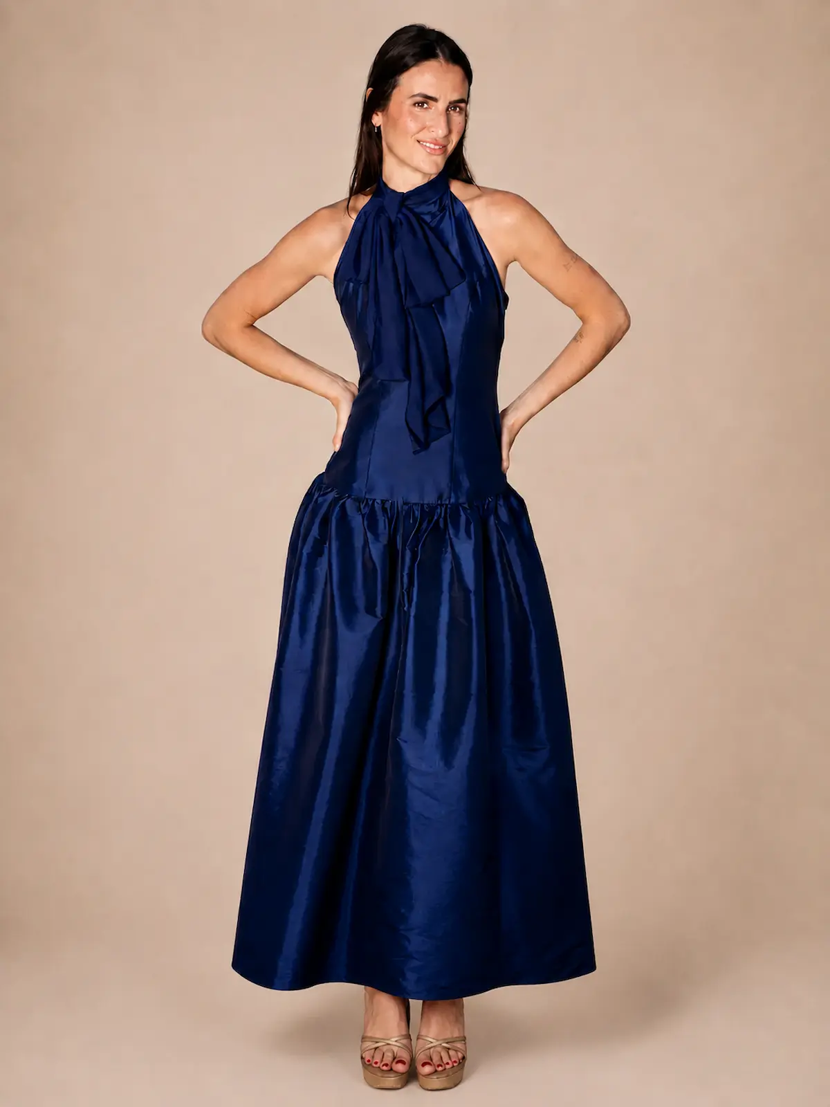 Vestido largo azul marino en tafetán con cuello halter y lazada. Su cuerpo estilizado y su amplia falda con volumen crean una silueta elegante y sofisticada, perfecta para bodas, graduaciones y eventos especiales.